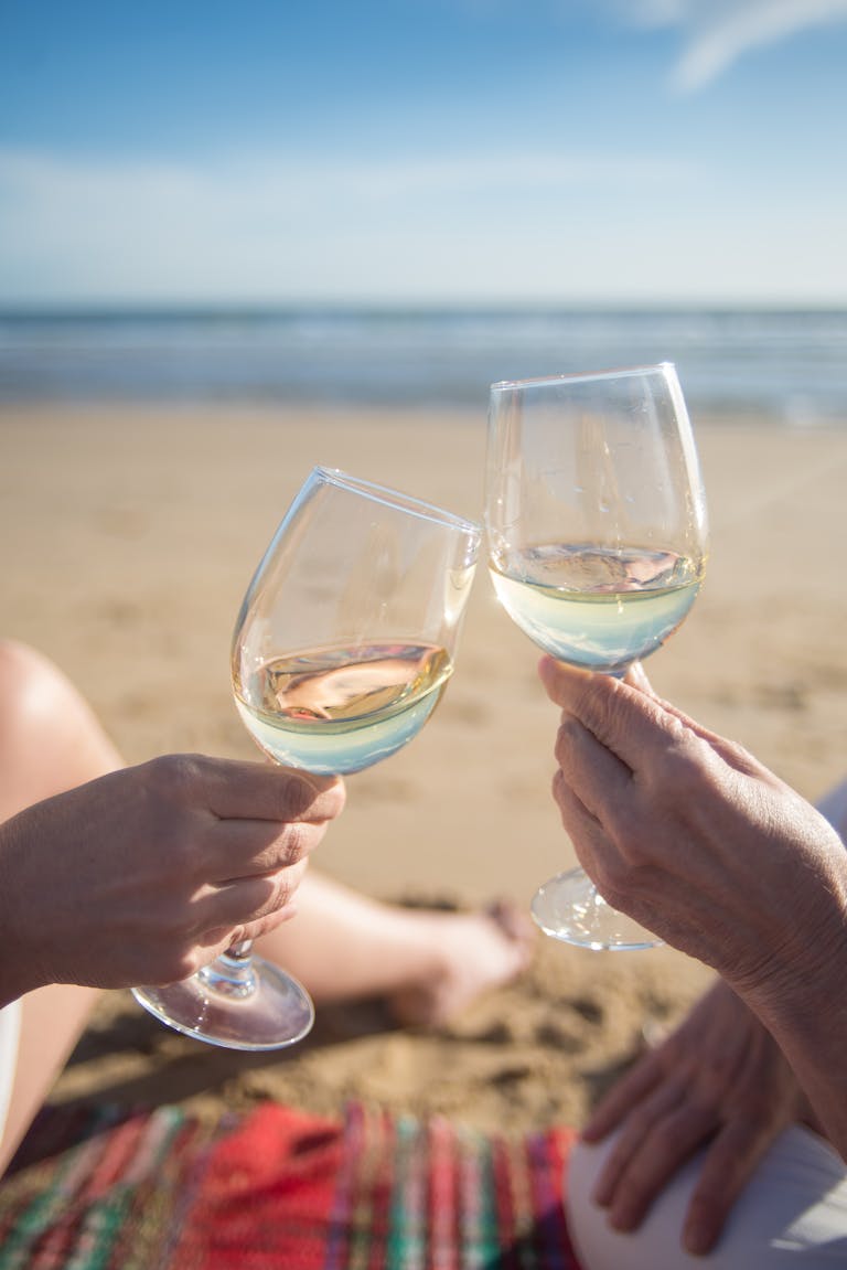 Close-up of two hands toasting wine glasses on a sunny beach in Portugal.