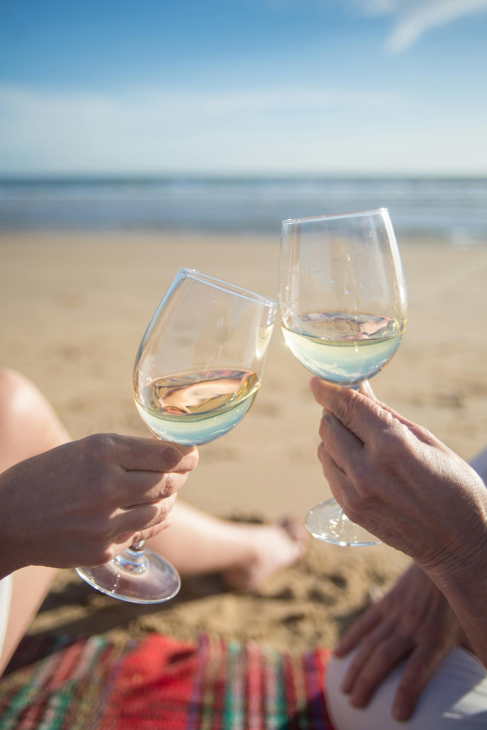 Close-up of two hands toasting wine glasses on a sunny beach in Portugal.